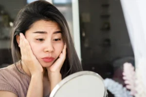 A woman with eye bags looking at her face in the mirror.