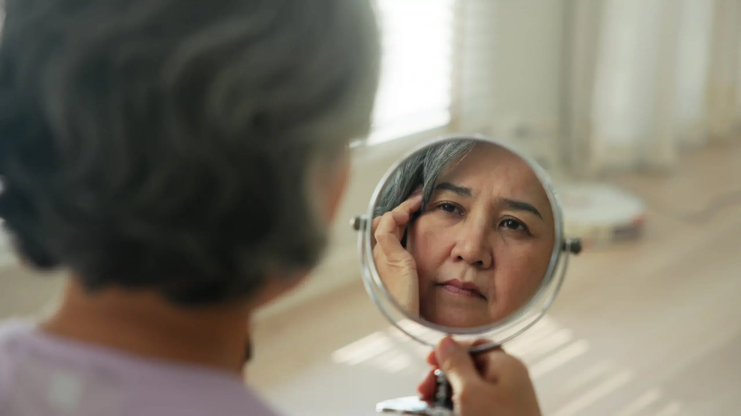 woman looking in the mirror and considering going for eye bag surgery in Singapore